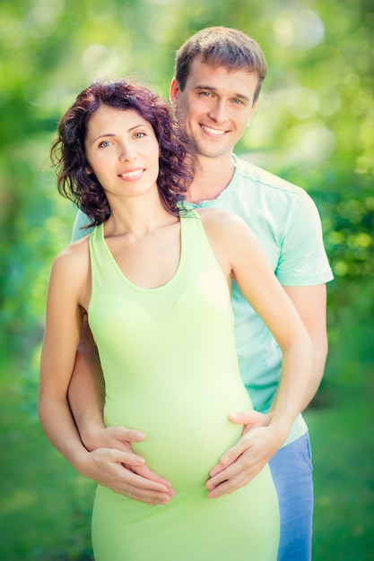 Hombre feliz abrazando el vientre de la mujer embarazada pareja divirtiéndose al aire libre en el parque de primavera el día de la madre