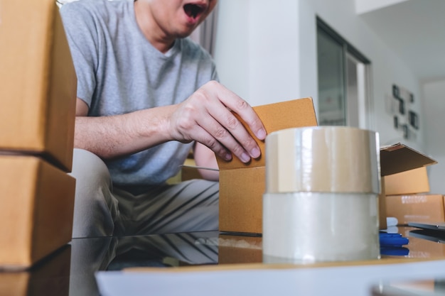 Hombre feliz abriendo la caja del paquete de compras en línea con paquete mientras está sentado en el sofá en casa