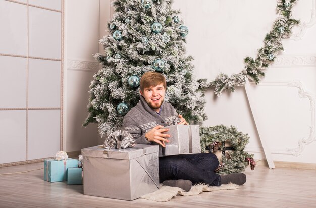 Hombre feliz abriendo un regalo en casa cerca del árbol de Navidad.