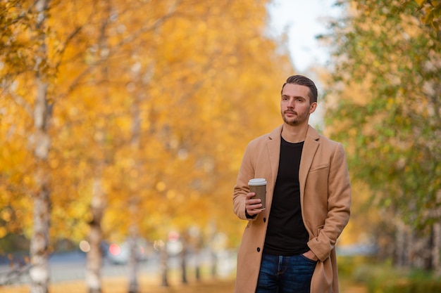 Hombre feliz en abrigo en otoño parque camina con café