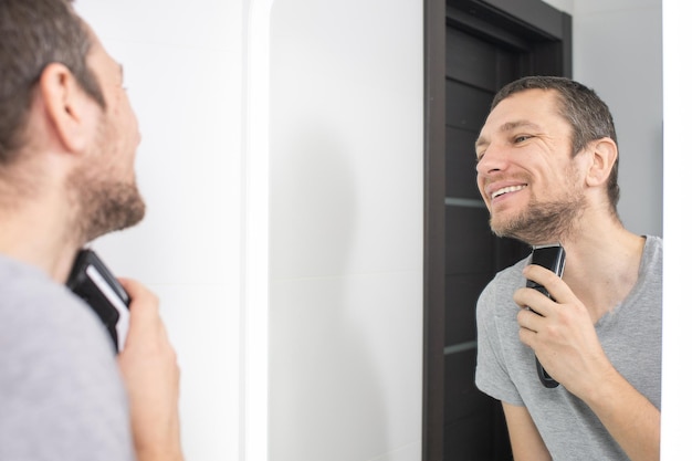 Un hombre feliz se afeita y se mira en el espejo.