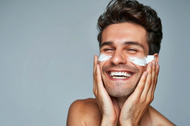 Hombre feliz aplicando loción después de afeitarse en la cara sobre un fondo gris