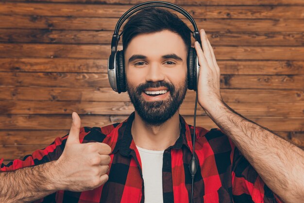 Hombre feliz en auriculares escuchando música y mostrando el pulgar hacia arriba