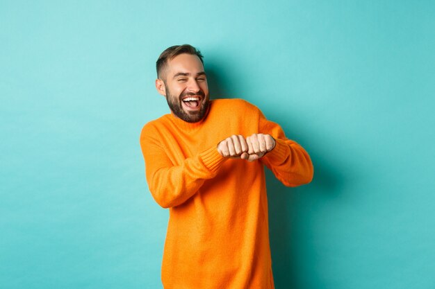 Hombre feliz bailando y celebrando el éxito, sintiéndose como ganador, sonriendo y regocijándose, fondo azul claro.