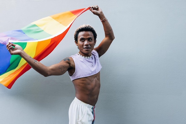 Hombre feliz con bandera arco iris de pie contra la pared