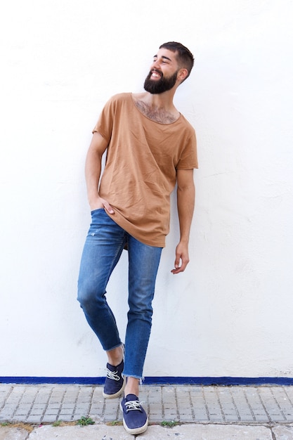 Hombre feliz con barba apoyada en la pared blanca