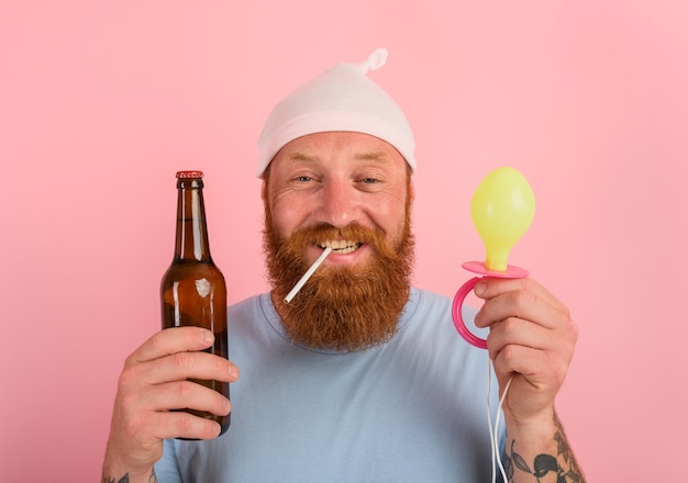 Hombre feliz con barba y tatuajes actúa como un bebé recién nacido con cerveza en la mano