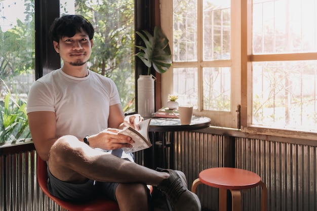 Hombre feliz beber café y libro de lectura en la cálida luz del verano