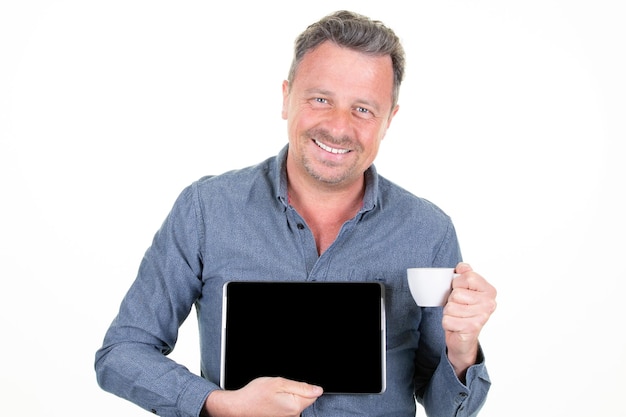 Hombre feliz bebiendo café presentando tablet pc pantalla vacía en fondo blanco.