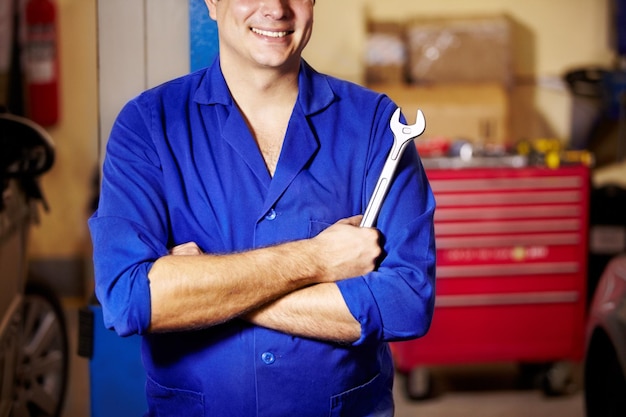 Hombre feliz brazos cruzados y manos de mecánico con llave para reparar mantenimiento y servicio de automóviles Técnico confiado llave inglesa y herramientas para arreglar inspección y profesional en el garaje o taller