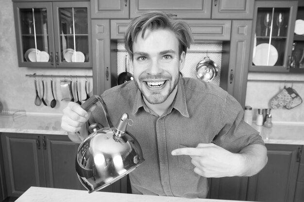 Hombre feliz con camisa azul apuntando con el dedo a la tetera Aparatos de cocina y muebles Preparación de alimentos Cocina Calefacción Agua hirviendo Hora del té Estado de ánimo del té Presentación de venta en línea del producto