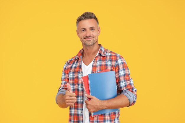 Hombre feliz en casual dando pulgar sosteniendo libros escolares educación de fondo amarillo