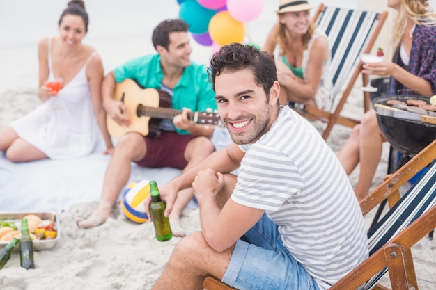 Hombre feliz con cerveza y sonriendo mientras está sentado con sus amigos