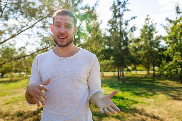 Hombre feliz con chaqueta blanca contándole una historia interesante a un amigo al aire libre en el parque de verano