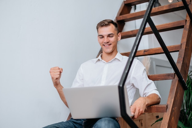 hombre feliz con una computadora portátil sentado en los escalones de su apartamento.