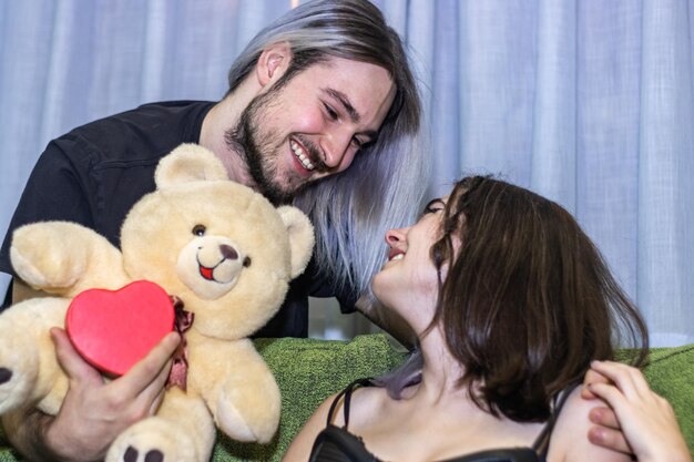 Foto hombre feliz dando un regalo a su pareja un hombre sosteniendo un oso de peluche junto a una mujer