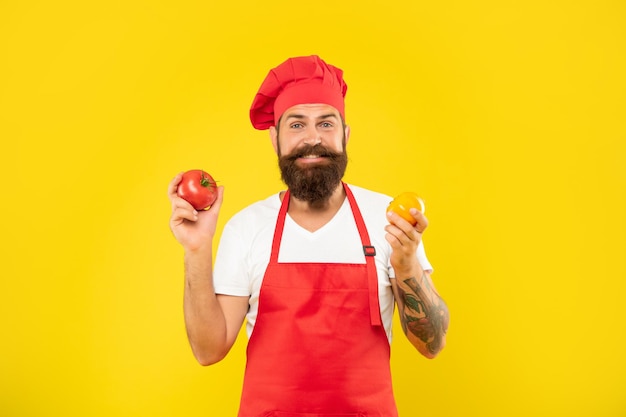 Hombre feliz en delantal de cocina y toque sosteniendo tomates rojos y amarillos chef de fondo amarillo