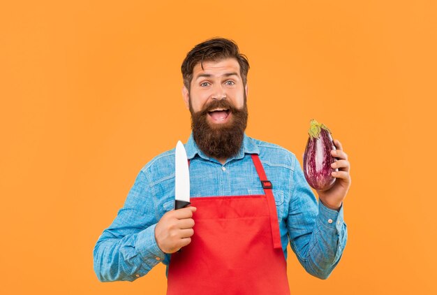 Hombre feliz en delantal con cuchillo de cocinero y cocinero de fondo amarillo berenjena