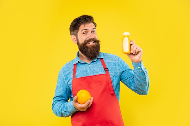 Hombre feliz en delantal con naranja y botella de jugo barman de fondo amarillo