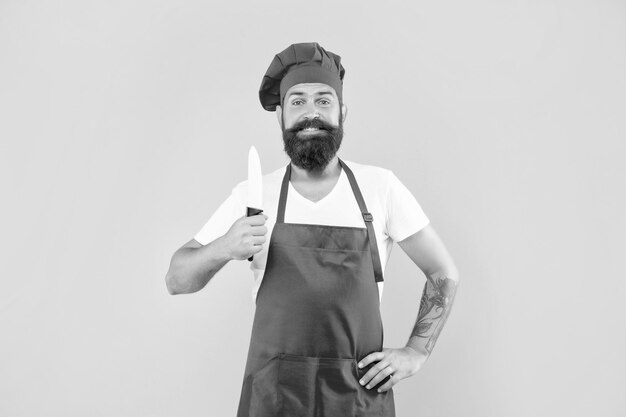 Hombre feliz en delantal rojo y toque con cuchillo de cocinero cocinero de fondo amarillo
