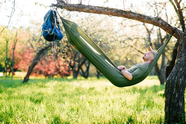 Hombre feliz descansando en una hamaca en el parque soleado