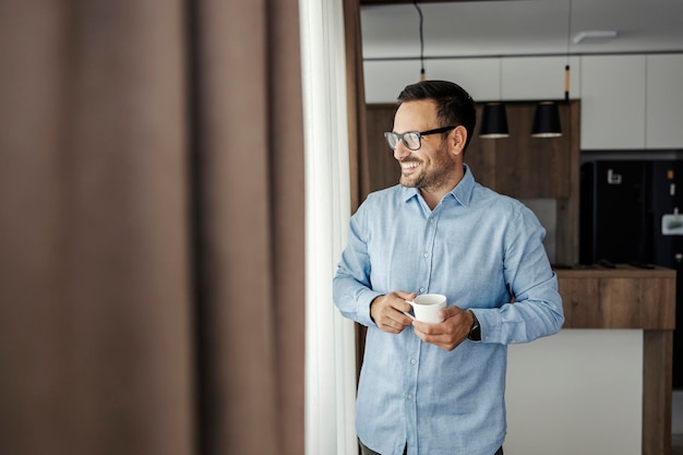 Un hombre feliz disfruta de un café mientras mira por la ventana