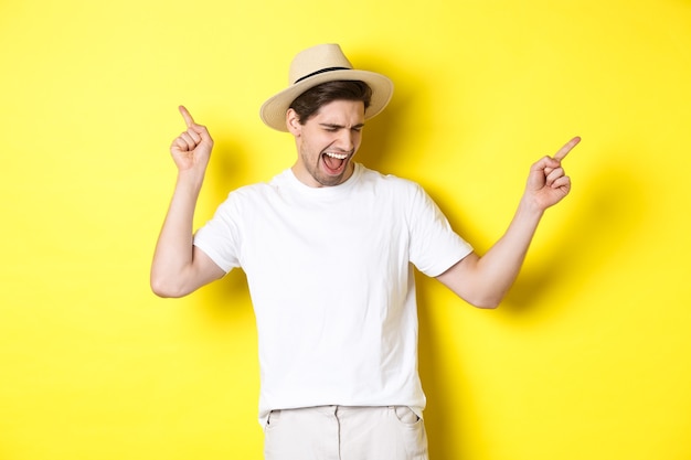 Hombre feliz disfrutando de vacaciones, turista bailando sobre pared amarilla