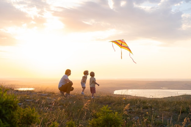 Hombre feliz y dos niños gemelos niños padre e hijos divirtiéndose con cometa en la naturaleza al atardecer