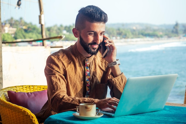 Hombre feliz egipcio con laptop hablando por teléfono en Goa