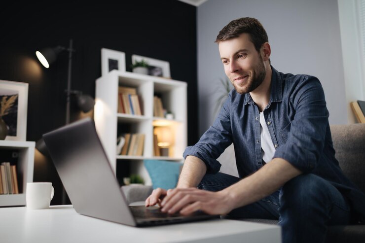 Hombre feliz escribiendo en la computadora portátil en el sofá