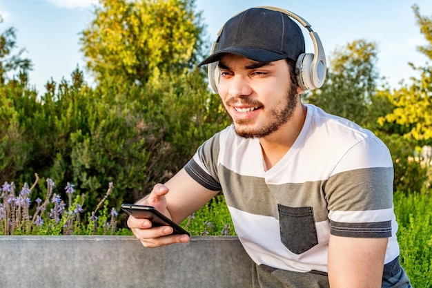 Hombre feliz escuchando música con auriculares en un banco en el parque de la ciudad