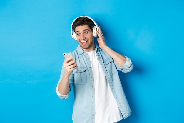 Hombre feliz escuchando música en auriculares y leyendo el mensaje en el teléfono inteligente