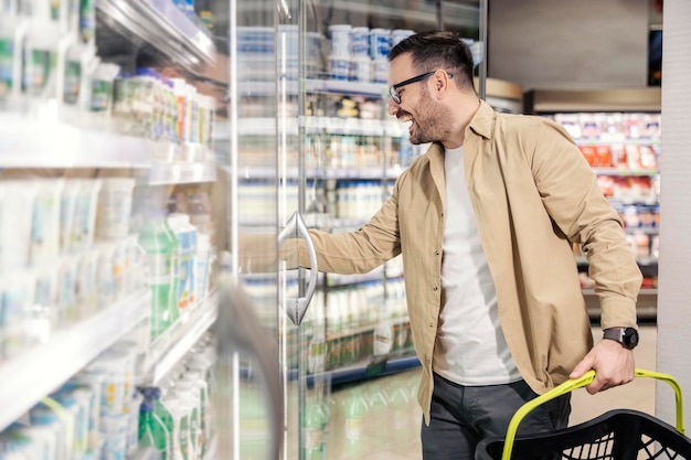 Un hombre feliz está sacando comestibles de la nevera en el supermercado y comprándolo