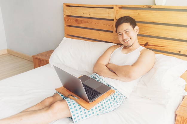 El hombre feliz está trabajando con su computadora portátil en su cama.