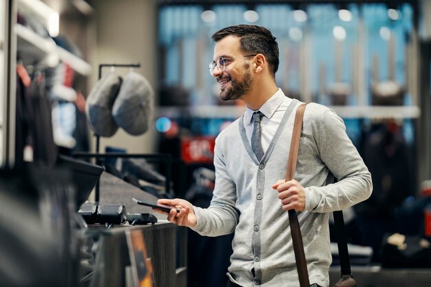 Un hombre feliz está usando un teléfono móvil para comprar sin efectivo en una boutique