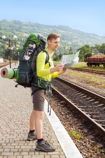 Hombre feliz excursionista con mochila leyendo el mapa en la estación de tren