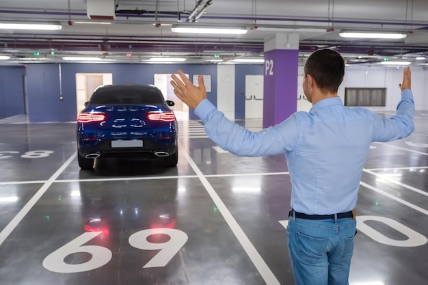 Foto hombre feliz en un fondo un auto nuevo en el estacionamiento subterráneo