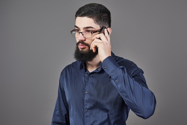 Hombre feliz con gafas habla por teléfono sobre fondo gris.