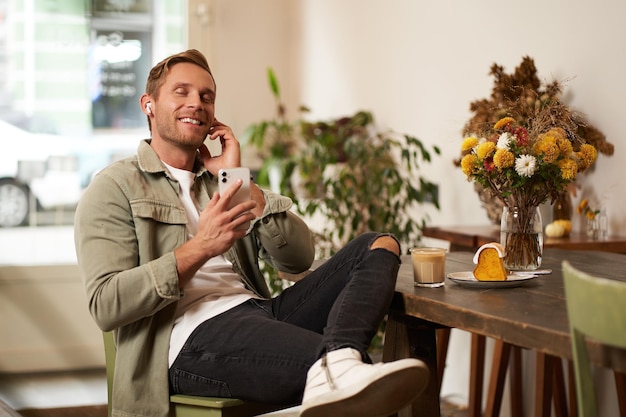 Hombre feliz y guapo en una cafetería escuchando música en auriculares inalámbricos se conecta al wifi de la cafetería para