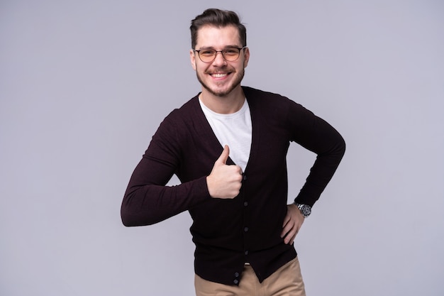 Hombre feliz hace un gesto con el pulgar hacia arriba, retrato sobre fondo gris.