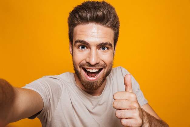 El hombre feliz hace un selfie por la cámara con los pulgares hacia arriba.