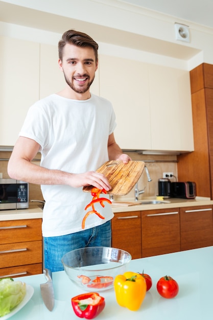 Hombre feliz haciendo ensalada en la cocina