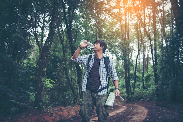 Hombre feliz hipster turista con mochila de agua potable mientras caminatas en el bosque de la naturaleza.