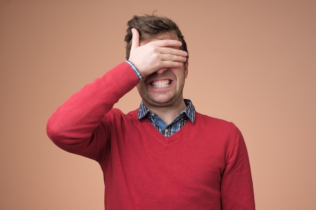 Hombre feliz joven que cubre los ojos con las manos