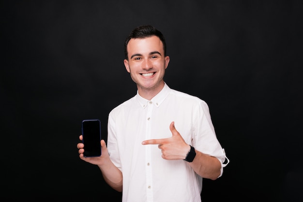 Hombre feliz joven que señala en la pantalla de su smartphone en fondo negro.