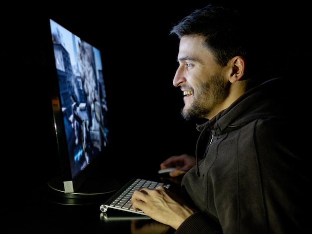 Hombre feliz jugando en una computadora de escritorio en una habitación oscura