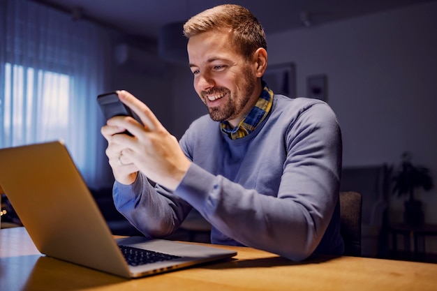 Un hombre feliz leyendo mensajes por teléfono en casa