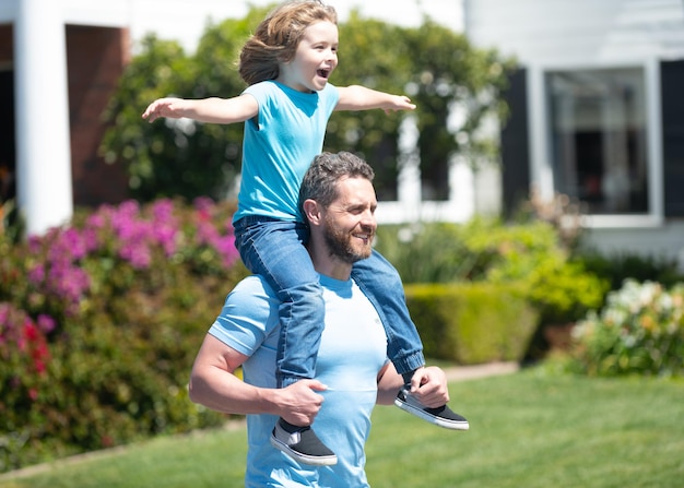 Un hombre feliz lleva a un hijo sentado sobre los hombros de los padres en verano al aire libre, a cuestas.