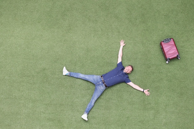 Foto hombre feliz con una maleta se encuentra en un césped verde