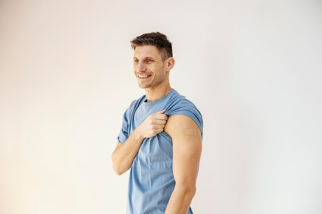 Foto un hombre feliz con la manga enrollada mostrando su hombro vacunado mientras sonríe